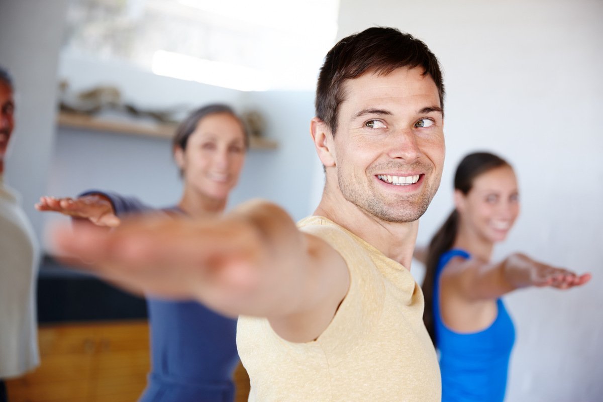Health, people and yoga with hands for balance, zen and wellness in studio. Smiling women, stretching men and warrior pose for fitness with spiritual, peaceful mindset and training in group class.